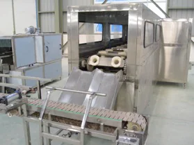 Large container feeding conveyor beside enclosed machinery