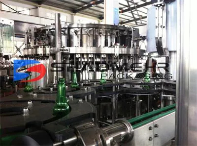 Green glass beer bottles beneath rotary filling heads